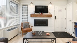 Una sala de estar con chimenea, televisor montado y una mesa de comedor con adornos.