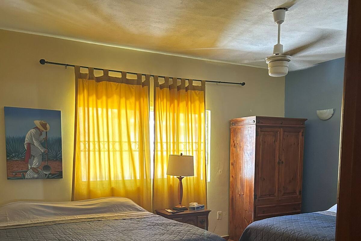 Une chambre avec deux lits, une armoire en bois, un tableau au mur et un ventilateur de plafond.