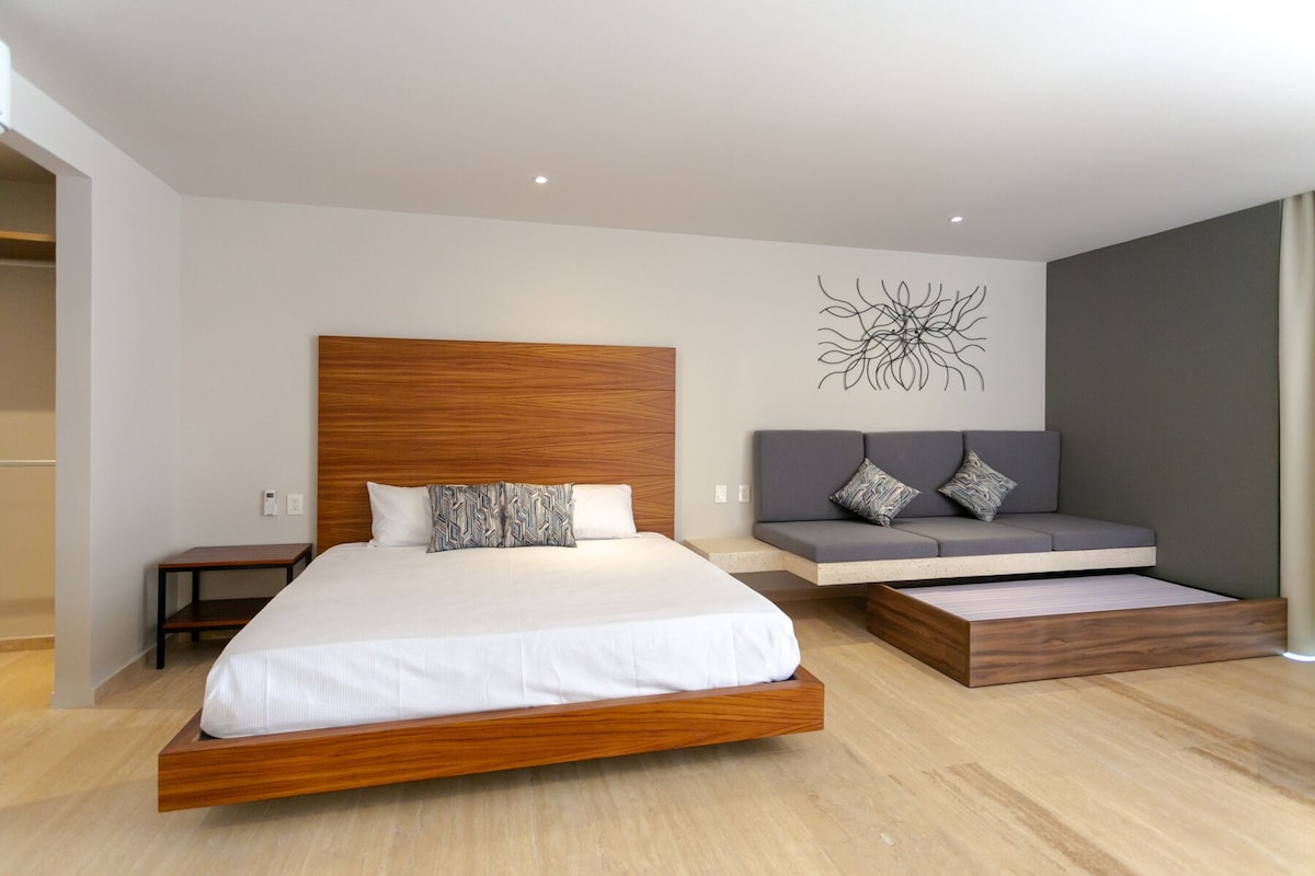 Quarto moderno com cama de madeira, sofá cinza e uma obra de arte na parede.