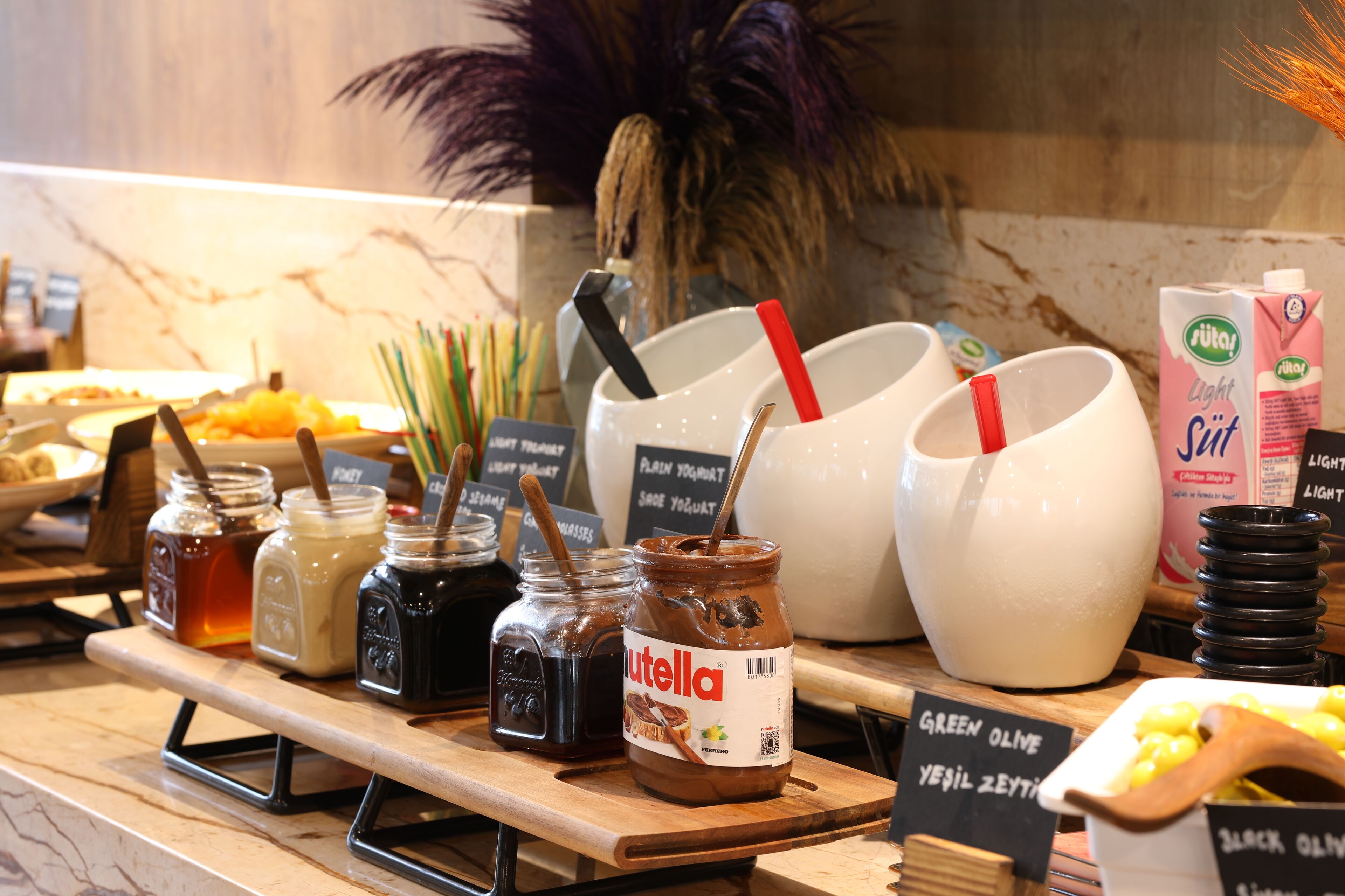 Un bufé con diversos alimentos y salsas, incluyendo frascos de miel, Nutella y pastas de aceitunas verdes y negras.