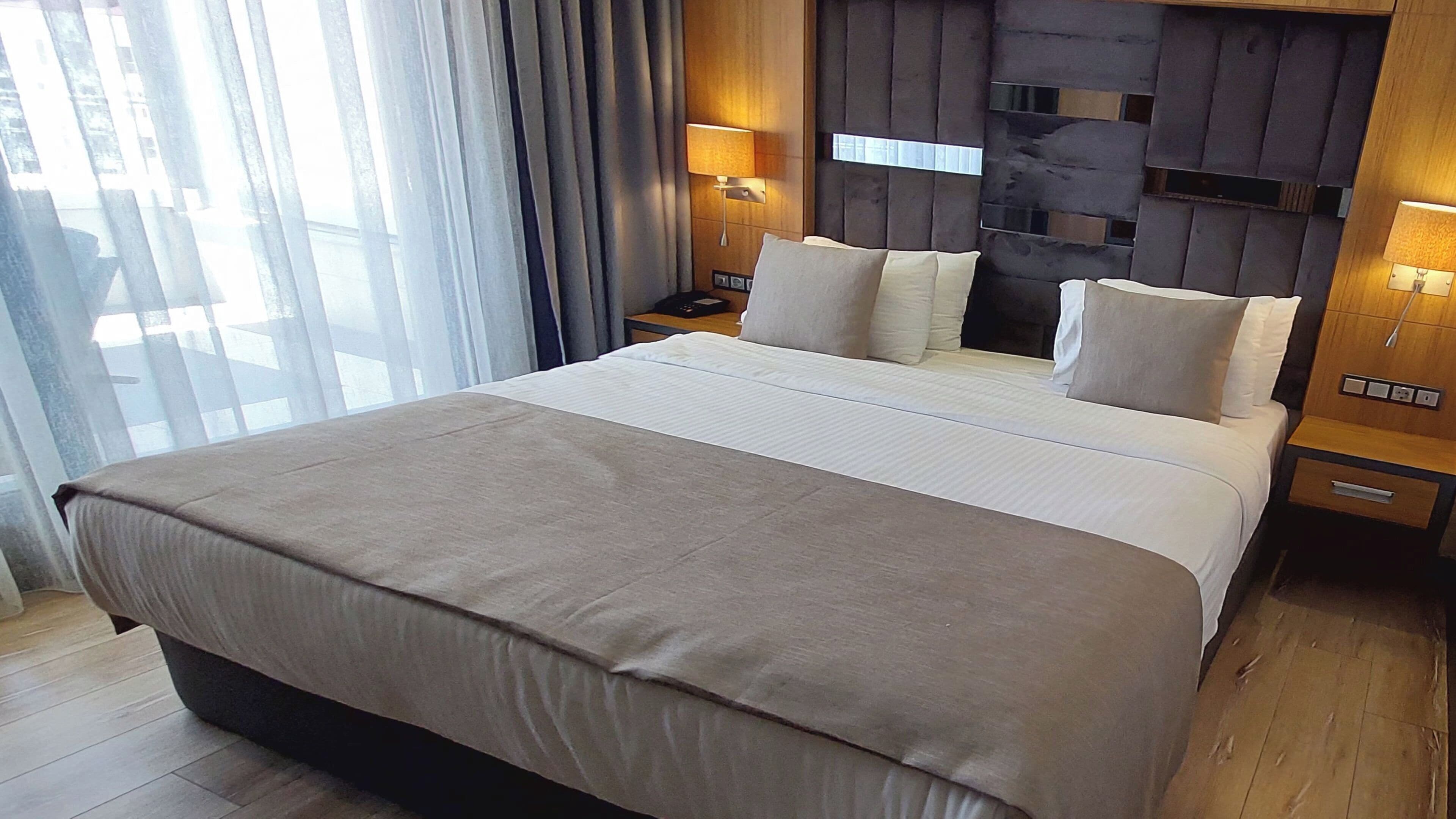 Habitación de hotel con una cama grande, dos mesitas de noche, cabecera con iluminación integrada y vistas al exterior a través del ventanal.