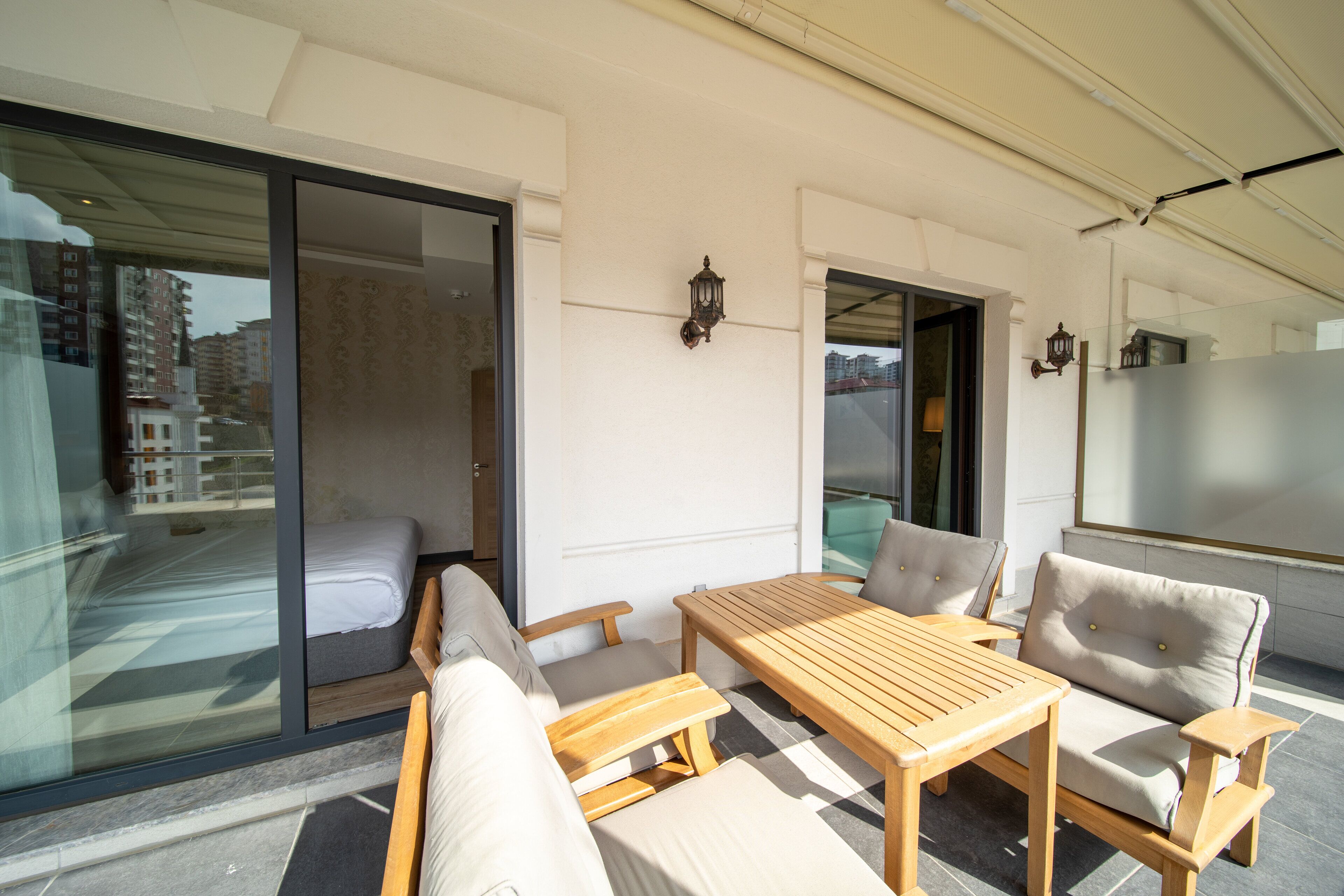 A balcony with a wooden table and four chairs, a sliding glass door, and two wall-mounted lanterns.
