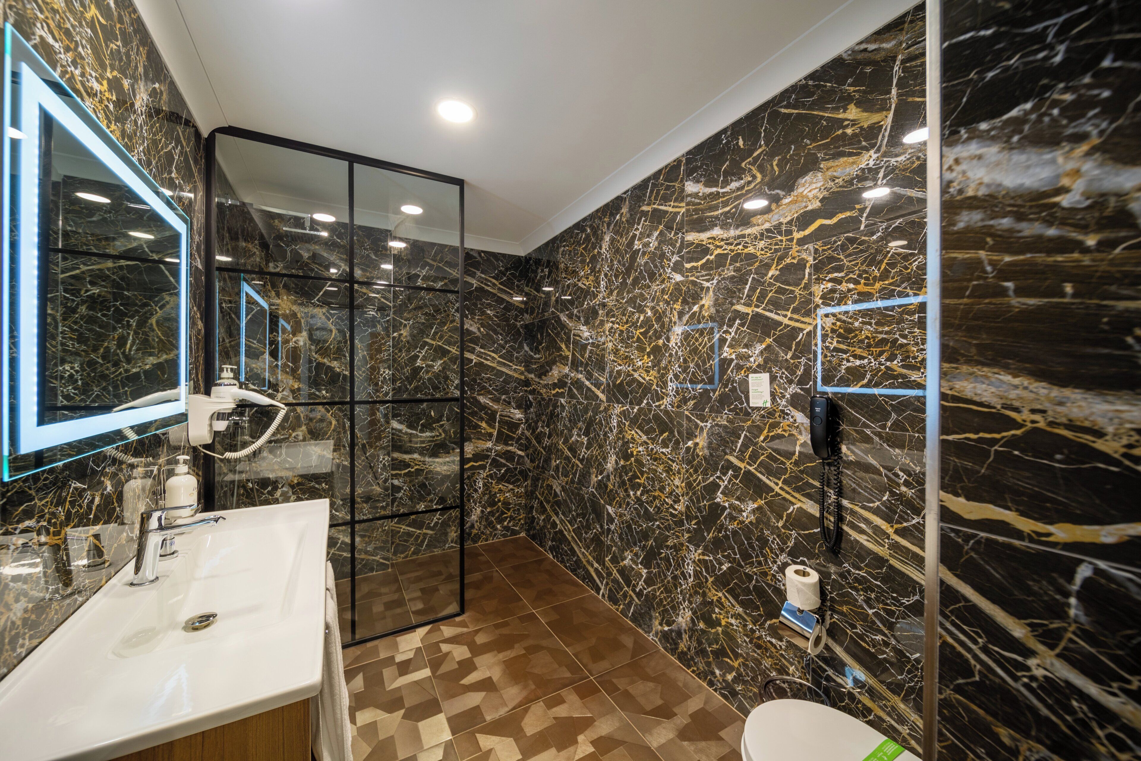 Un baño moderno con pared de mármol, cabina de ducha de vidrio y lavamanos con espejo.