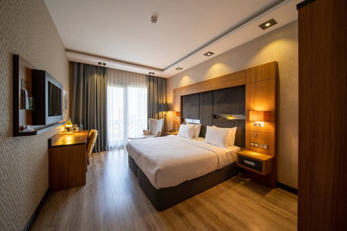 Une chambre d’hôtel avec un grand lit, un bureau avec une lampe, une télévision et une table de chevet avec une lampe.