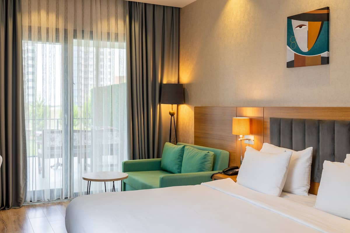 Une chambre d’hôtel avec un lit, un fauteuil vert, une petite table et une lampe.