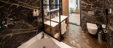 A modern bathroom with a marble wall, a bathtub, a sink, and a toilet.
