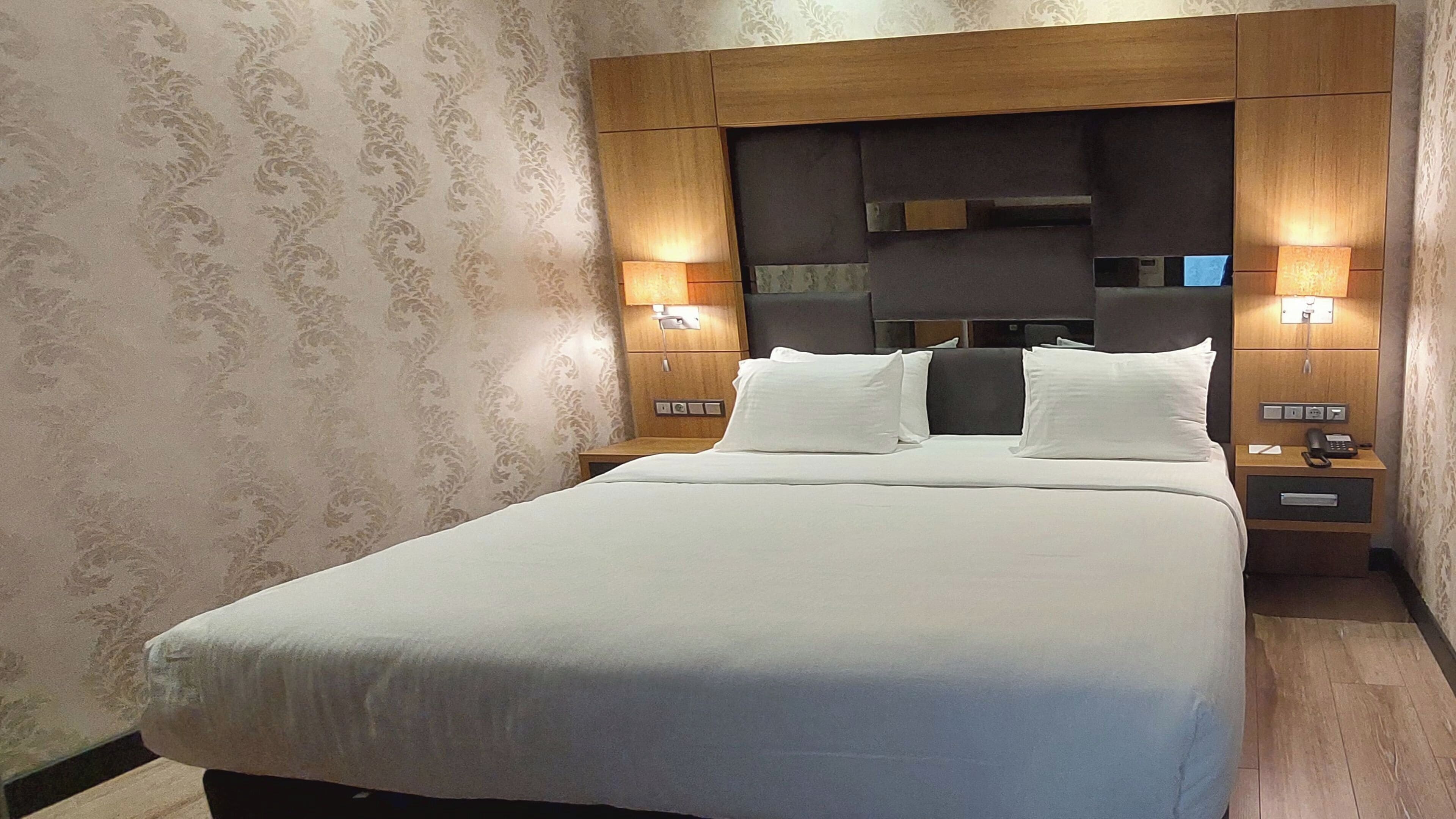 Habitación de hotel con una cama grande, dos mesitas de noche con lámparas y un cabecero con espejo.