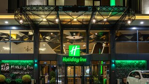 The exterior of a Holiday Inn with a modern design, featuring a prominent entrance, a covered walkway, and a green neon sign. - Holiday Inn Trabzon East by IHG (Yomra)