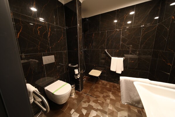 A modern bathroom with a toilet, bidet, and shower area, featuring dark marble walls and patterned flooring.
