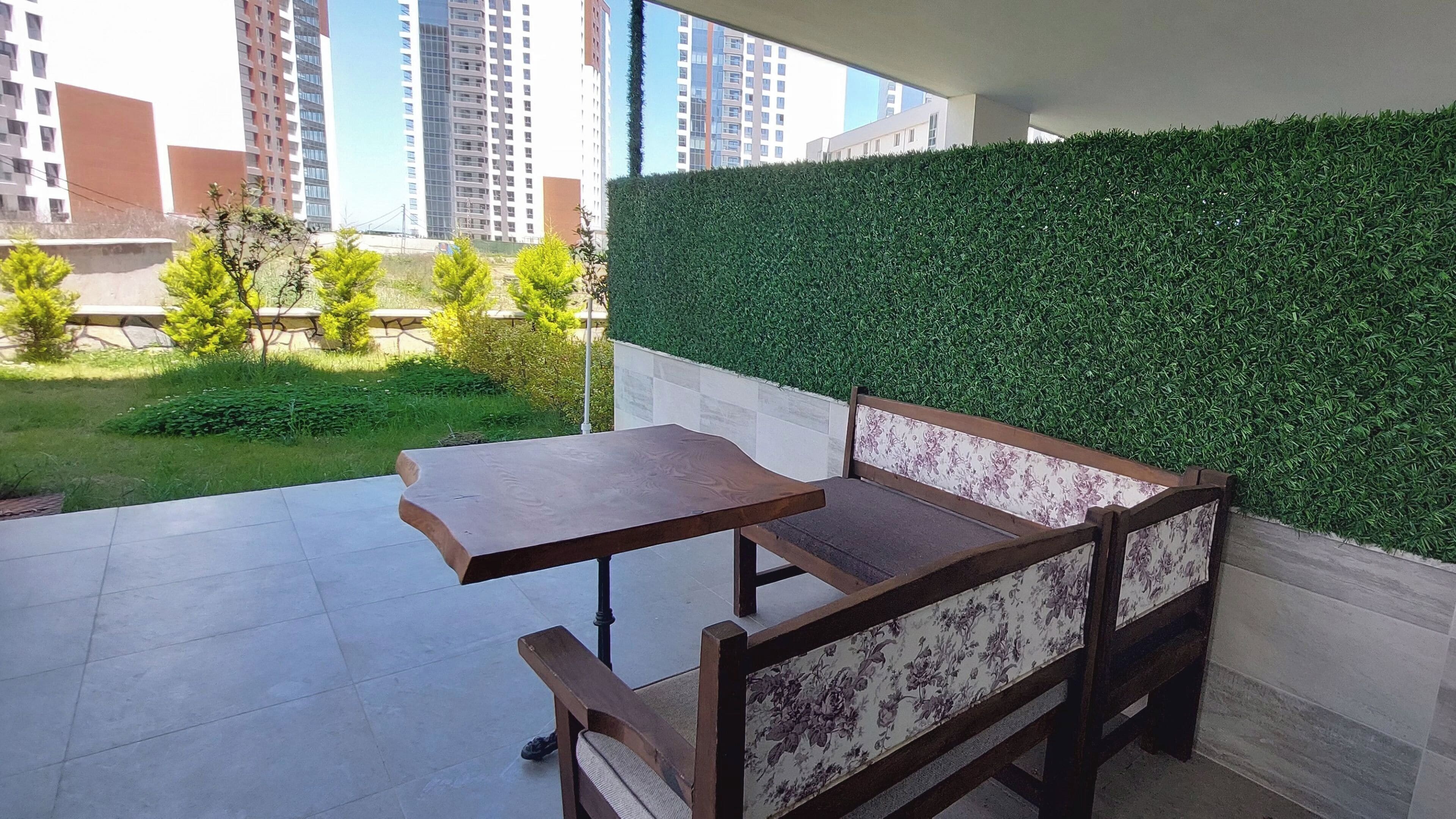 Un espace patio avec un banc et une table en bois, un mur végétal et une vue sur des immeubles de grande hauteur.
