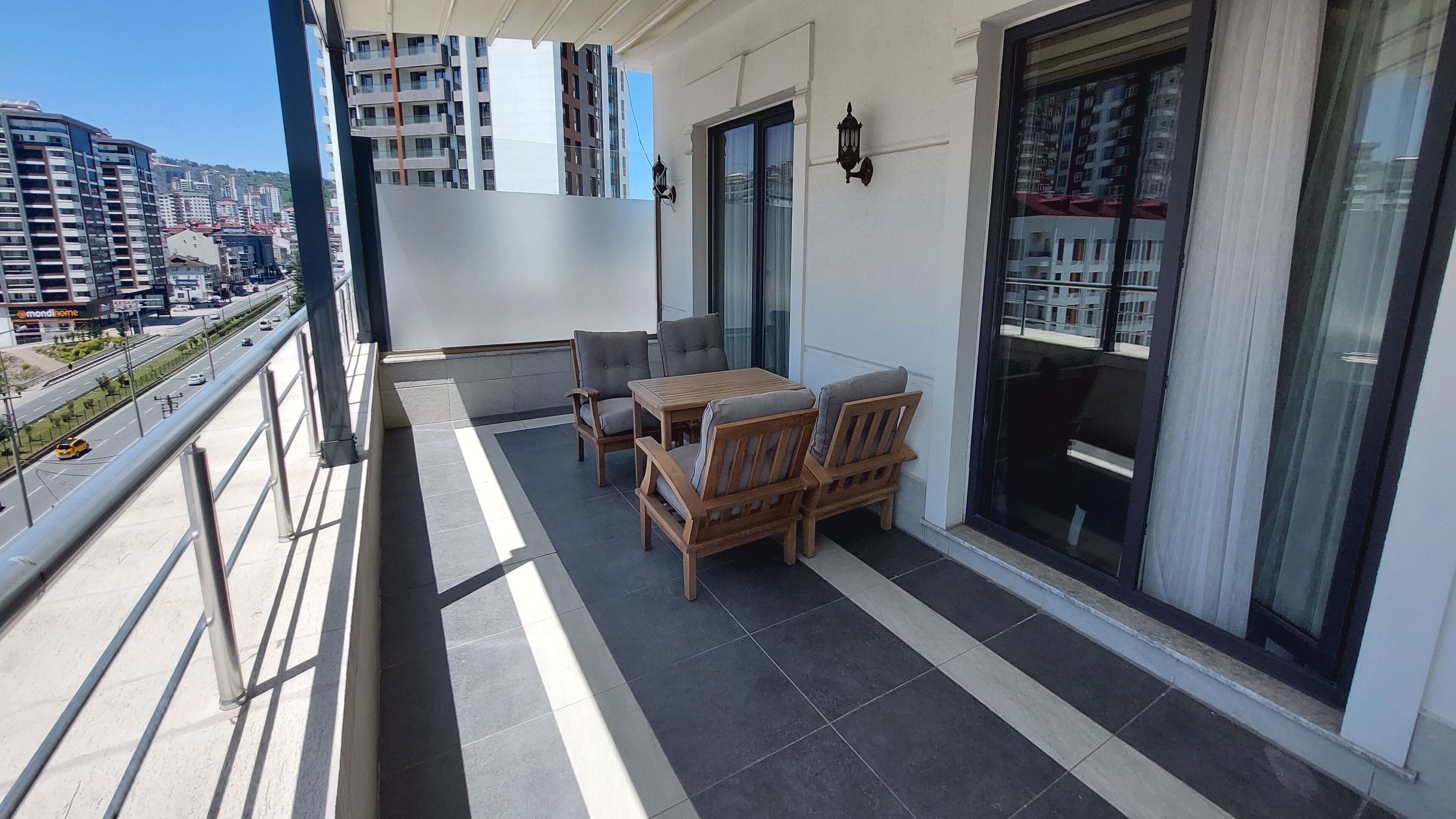 Un balcón con una mesa y sillas, vista panorámica de la ciudad y un edificio con amplios ventanales.