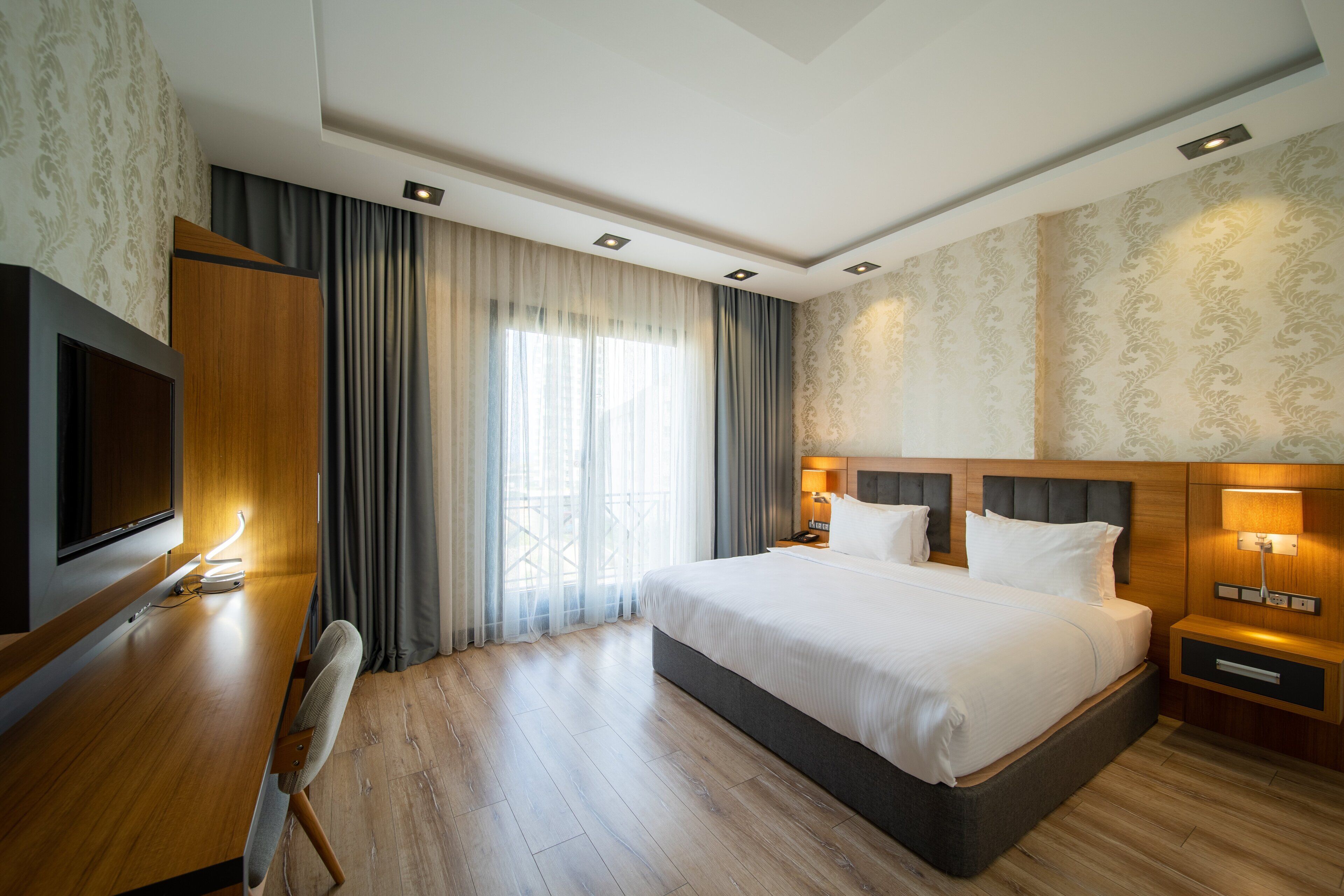 A hotel room with a large bed, a desk with a TV, and a window with curtains.