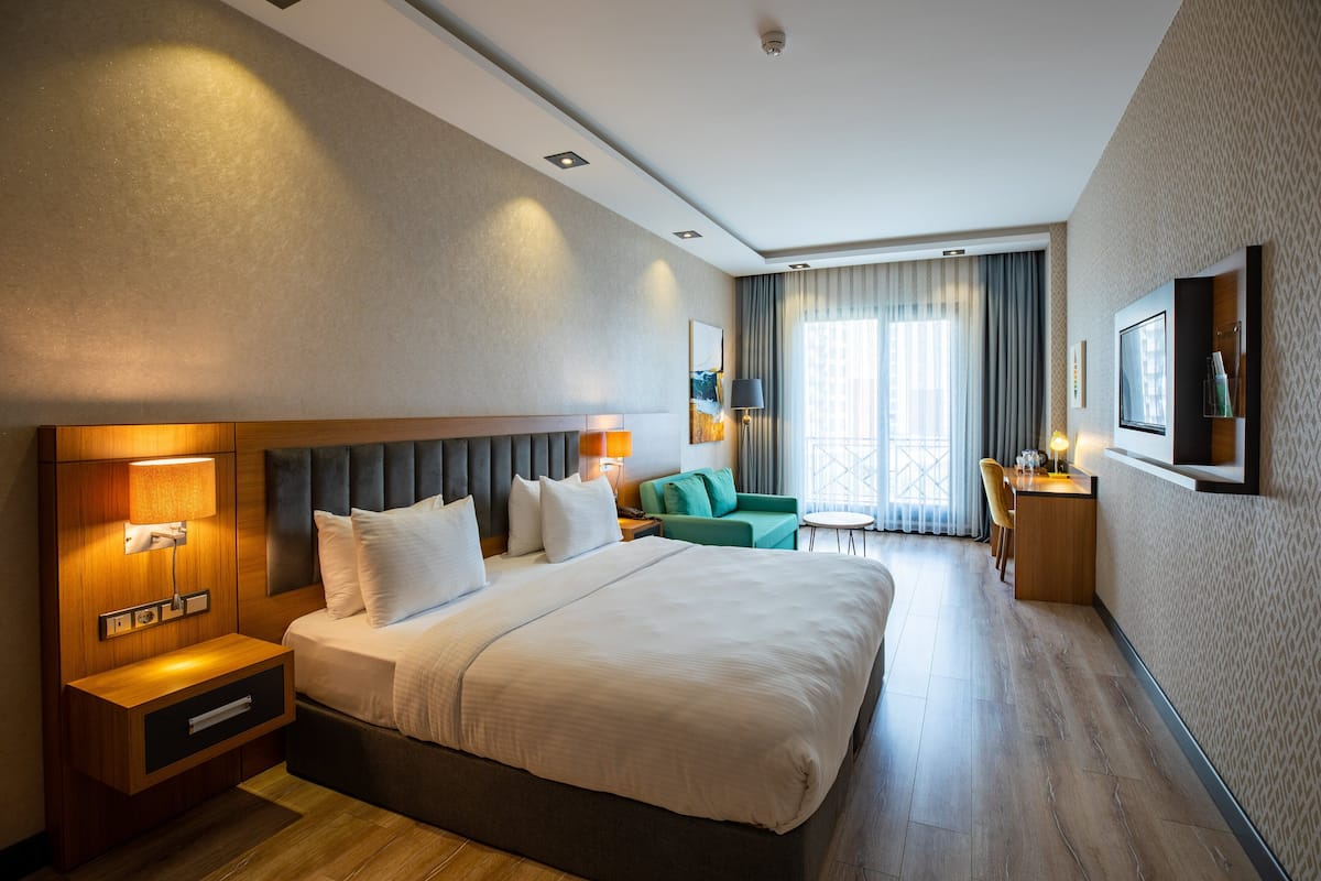 Une chambre d’hôtel avec un grand lit, des tables de chevet, un bureau, une chaise et une vue sur l’extérieur.