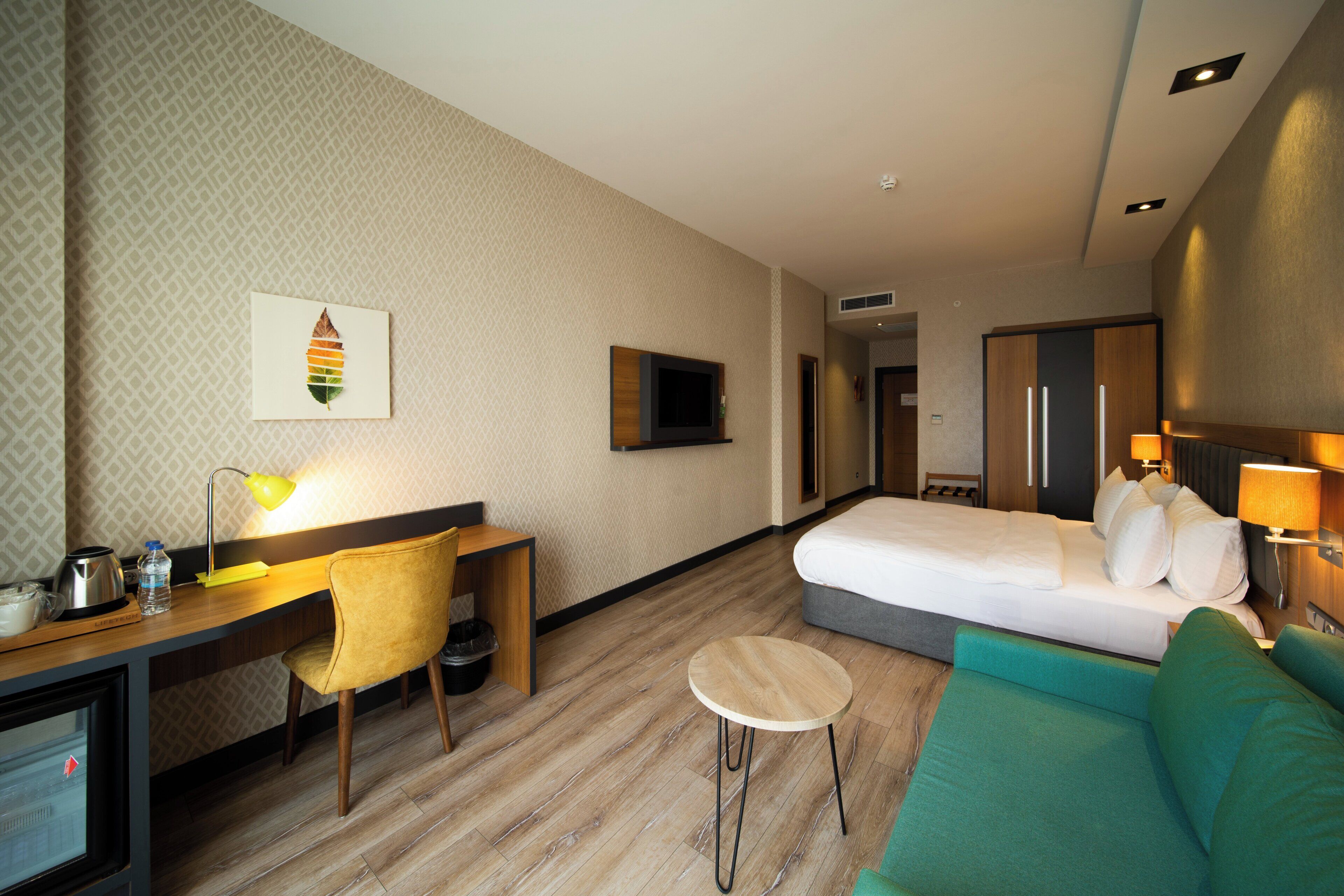 Habitación de hotel con cama, escritorio con silla, una mesita redonda y un sofá.