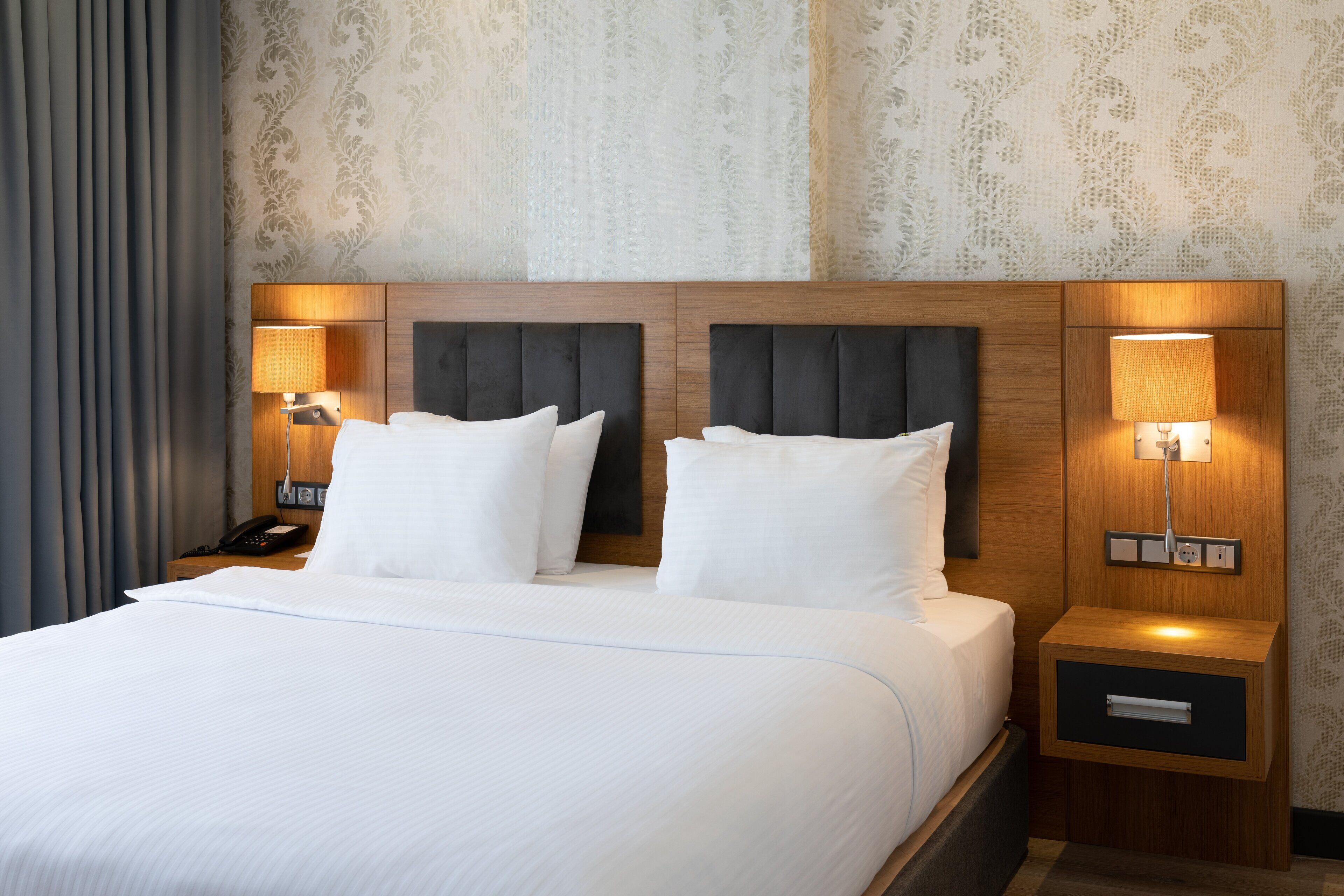 Una habitación de hotel con una cama grande, dos lámparas de noche, una mesita de noche y un teléfono.