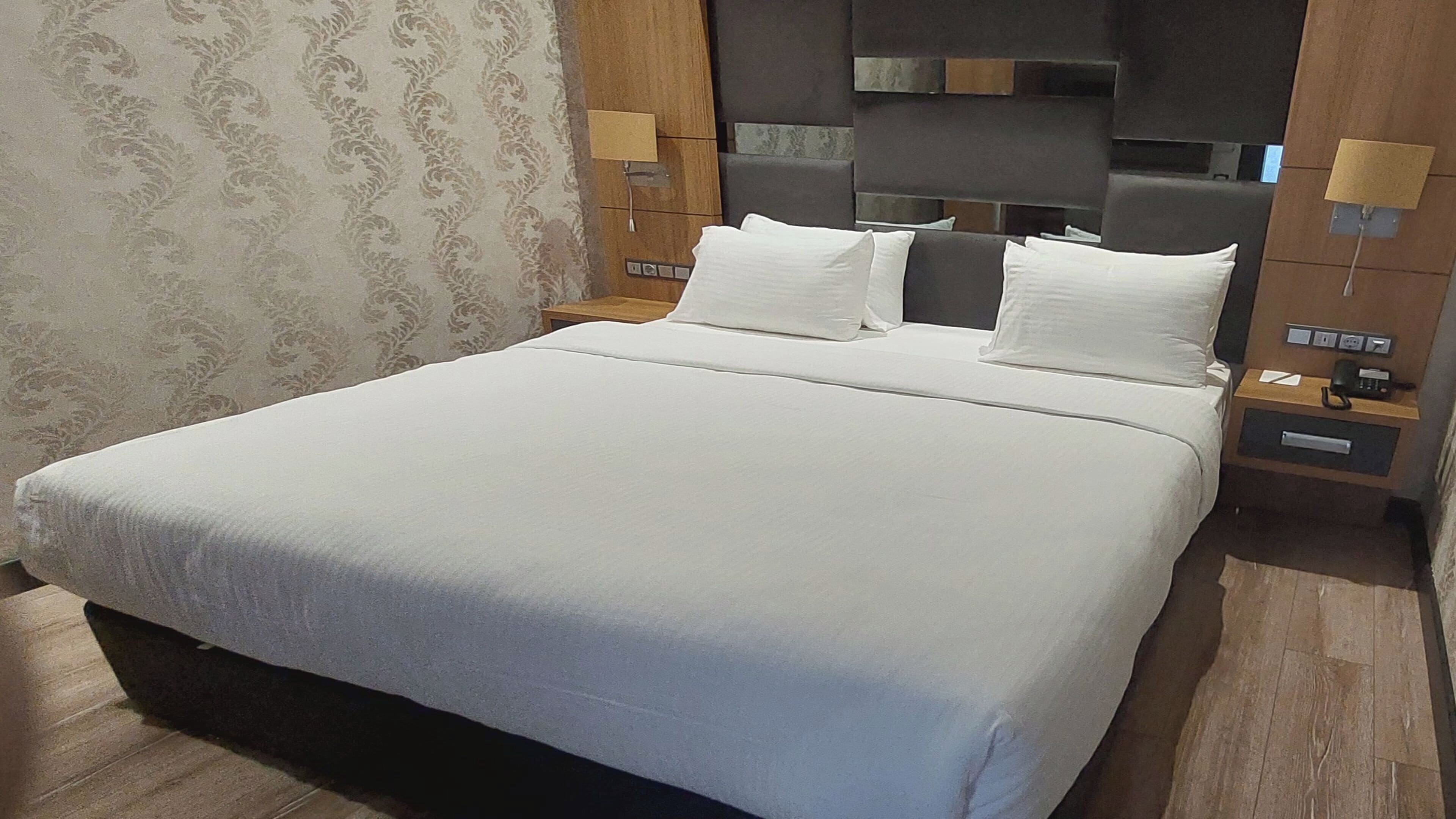 A hotel room with a large bed, two bedside tables, a headboard with a built-in shelf, and a patterned wallpaper.