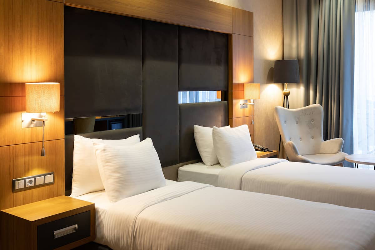 Une chambre d’hôtel avec deux lits, une chaise, un bureau avec une lampe et un téléviseur.