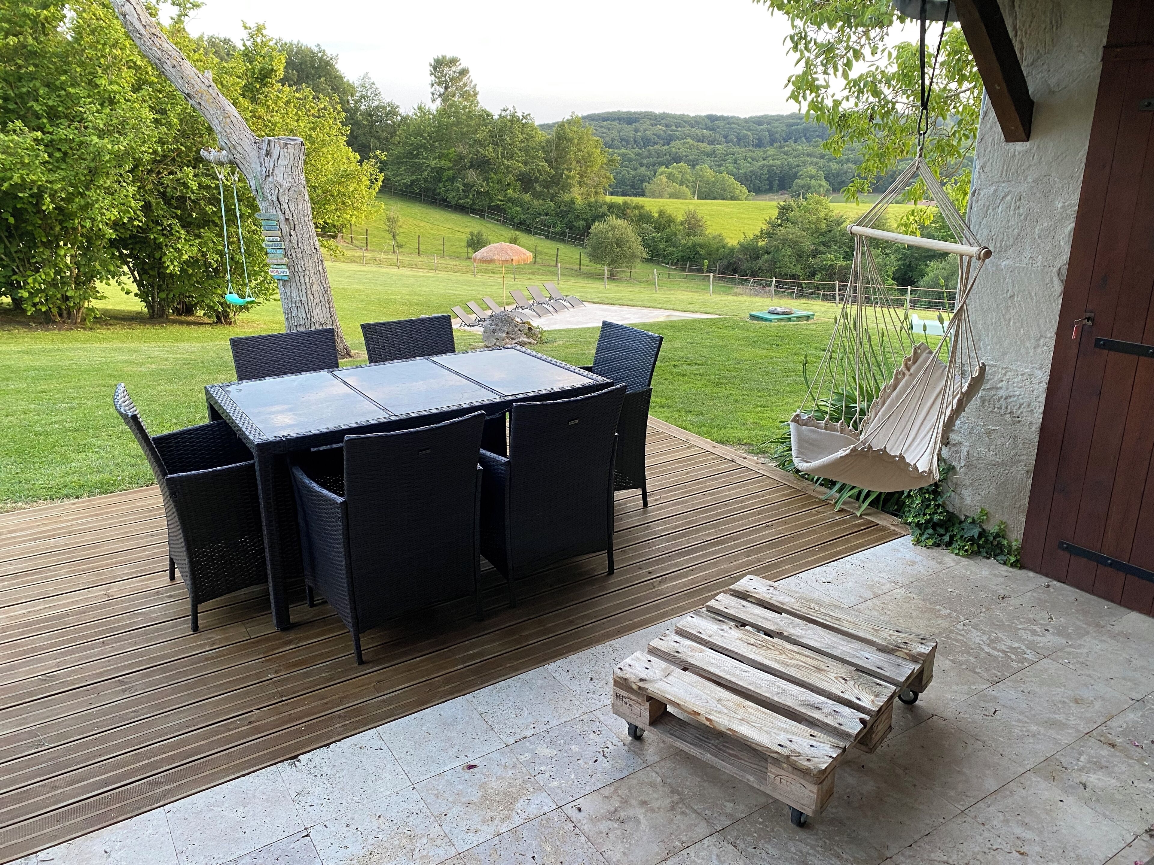 Een buitenpatio met een tafel en stoelen, een houten terras en een hangmat.