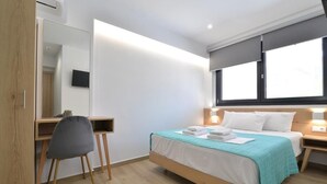 A modern hotel room with a bed, a desk, a chair, and a large window. - Anassa Suites (Dio-Olympos)