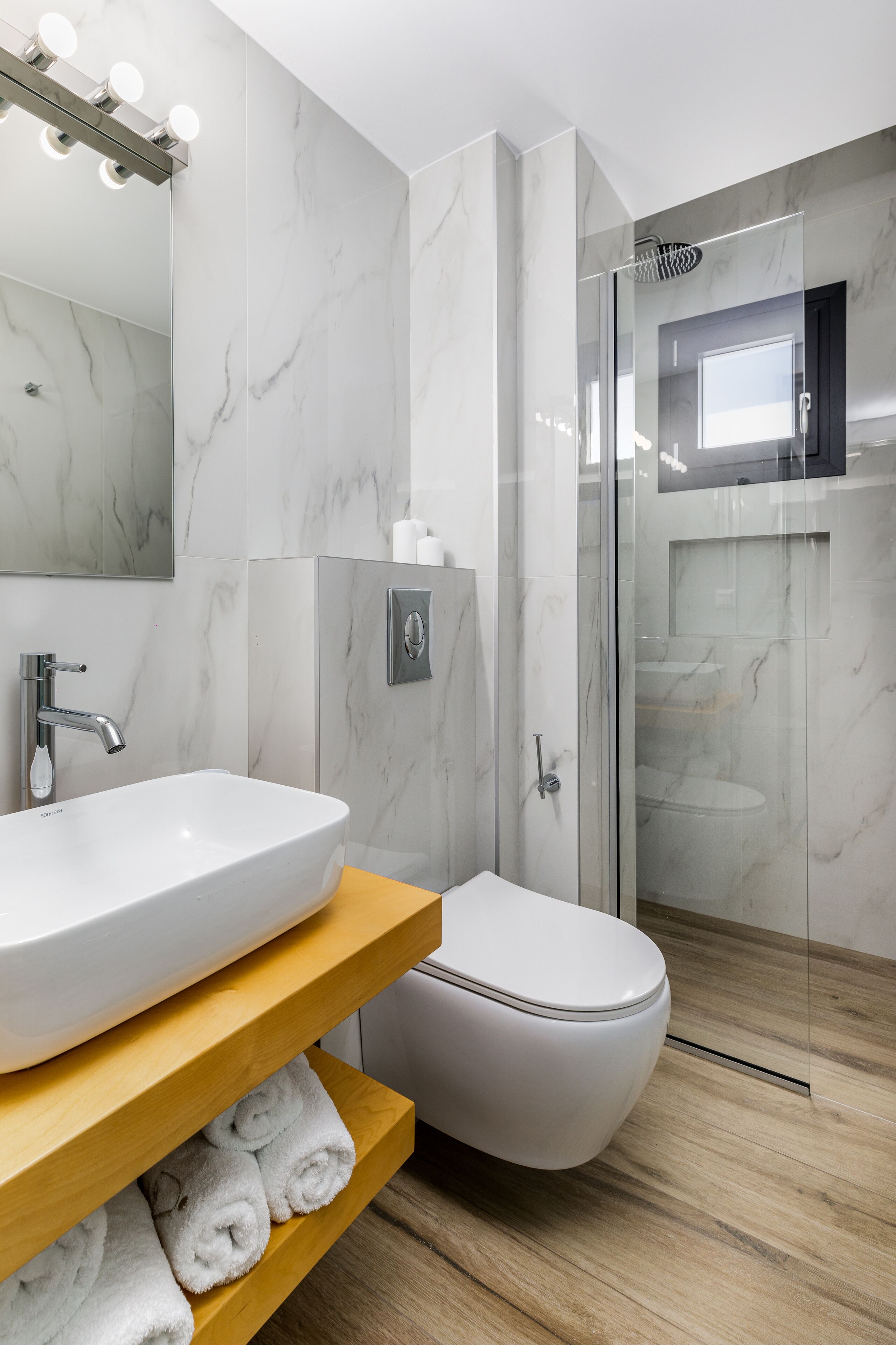 A modern bathroom with a marble sink, a toilet, and a glass-enclosed shower.