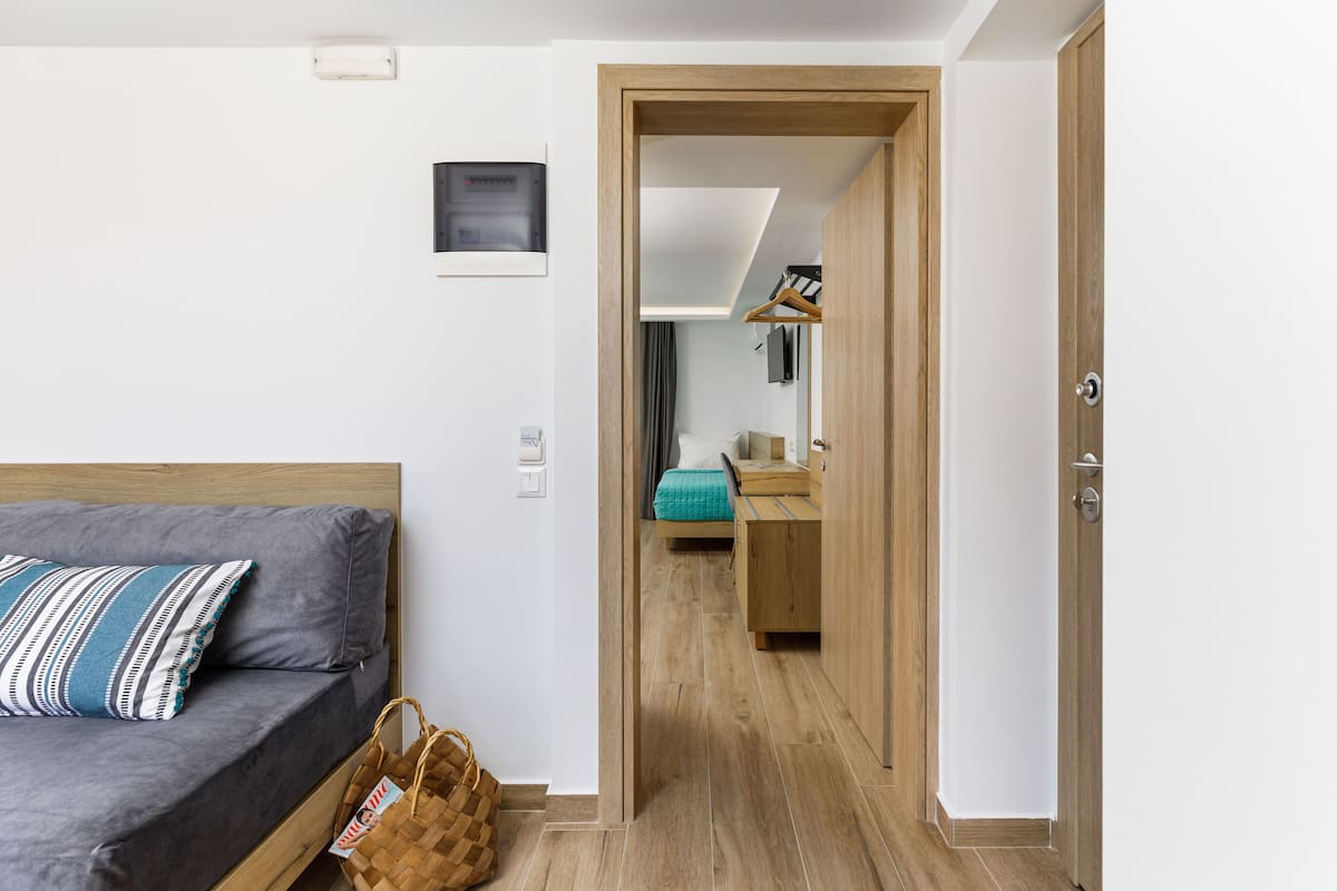 Una habitación con una cama, una puerta de madera, una mesita pequeña y un perchero.