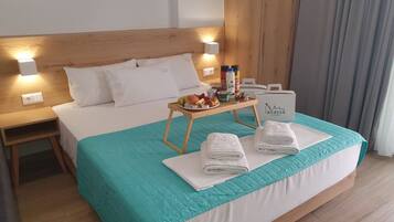 A hotel room with a bed, a nightstand, a tray table with breakfast items, and a sign for 'Anassa LE PIKOTARIA'.