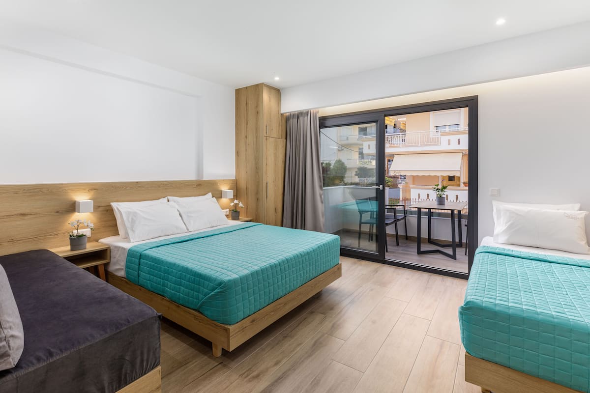Habitación de hotel con dos camas, cabecera de madera, balcón con mesa y sillas, y vista a la ciudad.