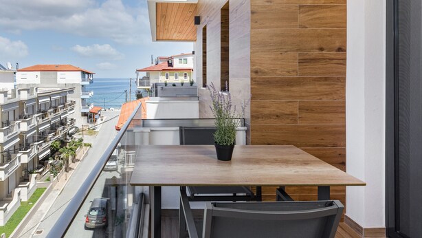 A balcony with a wooden table and chairs, overlooking a residential area and the sea. - Anassa Suites (Dio-Olympos)