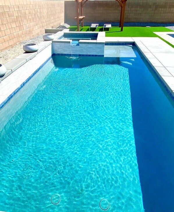 Piscina retangular com água azul cristalina, cercada por um deck ladrilhado e um muro de tijolos.