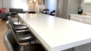 Et moderne køkken med en stor ø, sorte stole og en grå sofa i baggrunden.