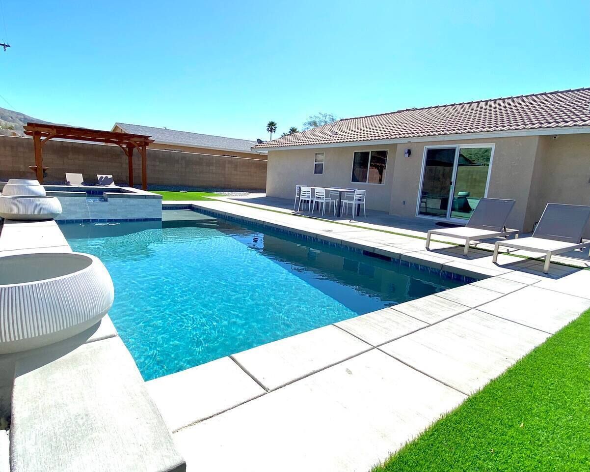 Un jardin avec une piscine, une pergola et un petit bâtiment doté d’un toit en tuiles.