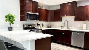 Une cuisine moderne avec des meubles en bois foncé, des appareils en acier inoxydable, un plan de travail blanc et un tabouret de bar.