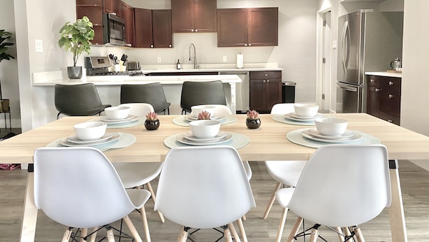Une cuisine moderne avec des meubles en bois foncé, un réfrigérateur en acier inoxydable et un coin repas comprenant une table en bois et des chaises blanches.