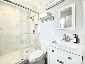 A bathroom with a glass shower enclosure, a white toilet, a sink with a mirror above it, and a bottle of soap on the sink. - Spring Sale New Pool Spa (Scottsdale)