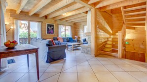 A spacious log cabin interior with a large sofa, a dining table, and a staircase. - Alptitude Chalet Largo - spacious detached chalet (Morzine)