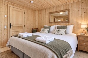 A wooden-paneled bedroom with a bed, pillows, a bedside table, and a mirror.