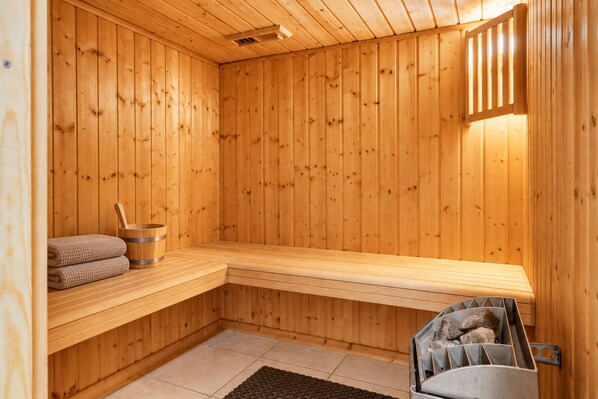 A wooden sauna with benches, a bucket, and a stone-filled container.