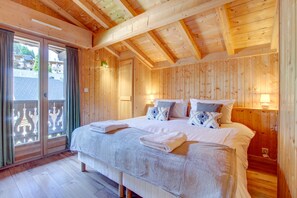 Een slaapkamer met houten lambrisering, een groot bed, twee bedlampjes en een uitzicht door een schuifdeur.