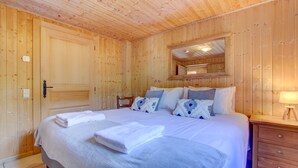 A wooden-paneled room with a bed, a nightstand, a mirror, and a door. - Alptitude Chalet Largo - spacious detached chalet (Morzine)