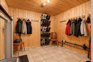 A room with wooden walls, a tiled floor, and a shoe rack with various footwear.