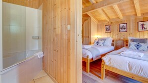 A wooden cabin bedroom with two beds, a wooden ceiling, and a bathroom with a shower. - Alptitude Chalet Largo - spacious detached chalet (Morzine)