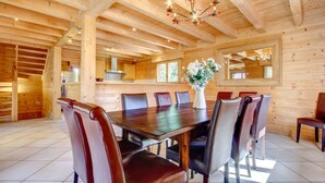 A wooden interior with a dining table surrounded by chairs, a chandelier, and a kitchen area visible through an open door. - Alptitude Chalet Largo - spacious detached chalet (Morzine)