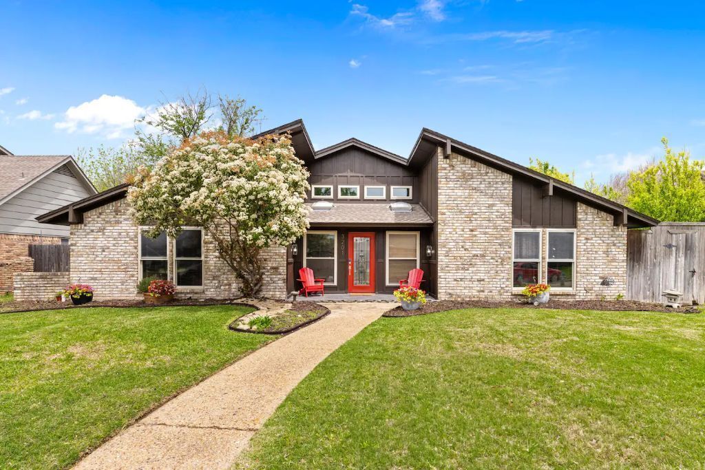 A two-story house with a stone facade, a red front door, and a small front yard with a pathway leading to the entrance.