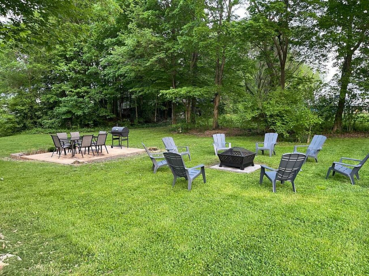 Un espace extérieur aménagé avec des chaises et une table, entouré d’une pelouse verdoyante et d’arbres.