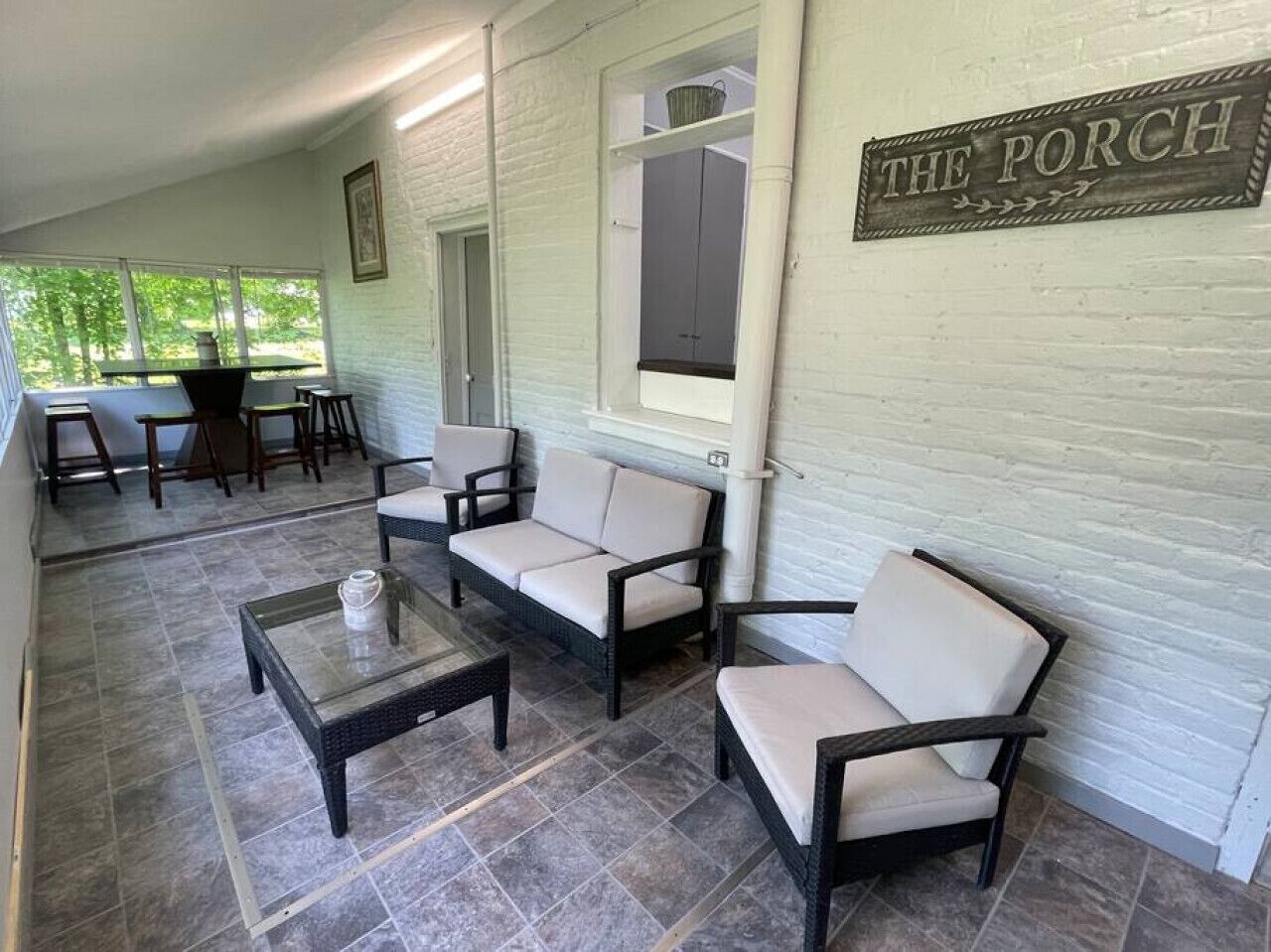 A covered patio area with outdoor seating, a sign reading "THE PORCH," and a view of the outdoors.