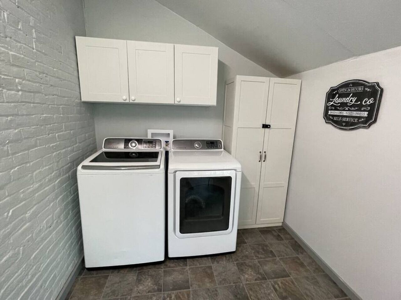 Een wasserette met twee witte wasmachines, een droger en een kast.