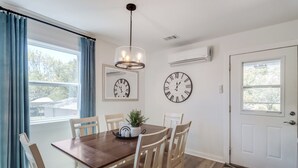 Un coin repas avec une table en bois, des chaises de couleur beige, un lustre et deux horloges murales.