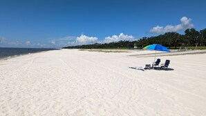 Une vaste plage de sable fin, avec quelques chaises de plage et un parasol bleu.
