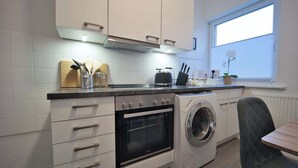 Una cocina compacta con horno integrado, lavadora y ventana con persianas.
