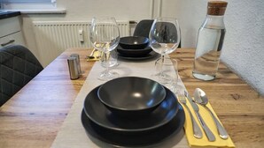 Una mesa de comedor servida con platos negros, copas de vino, cubiertos y una botella de agua.